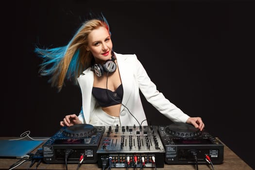 Beautiful blonde DJ girl in a white suit on decks on the party on the black background