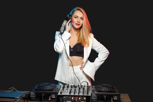 Beautiful blonde DJ girl in a white suit on decks on the party on the black background