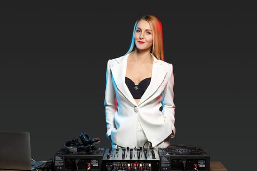 Beautiful blonde DJ girl in a white suit on decks on the party on the black background