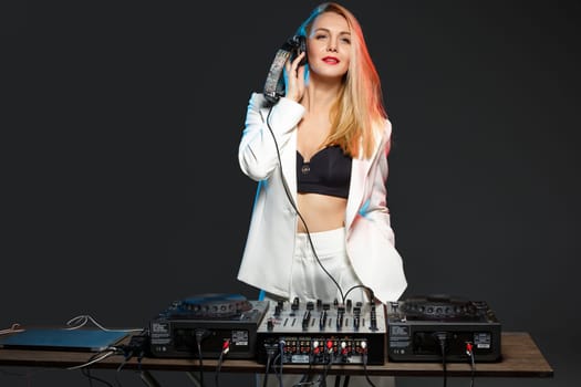 Beautiful blonde DJ girl in a white suit on decks on the party on the black background