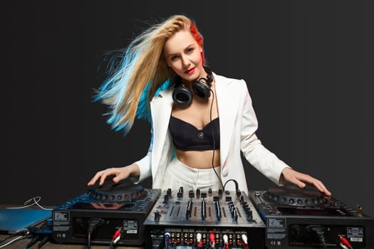 Beautiful blonde DJ girl in a white suit on decks on the party on the black background