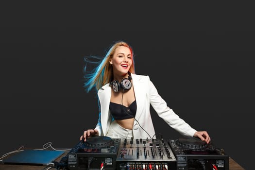 Beautiful blonde DJ girl in a white suit on decks on the party on the black background