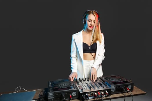 Beautiful blonde DJ girl in a white suit on decks on the party on the black background