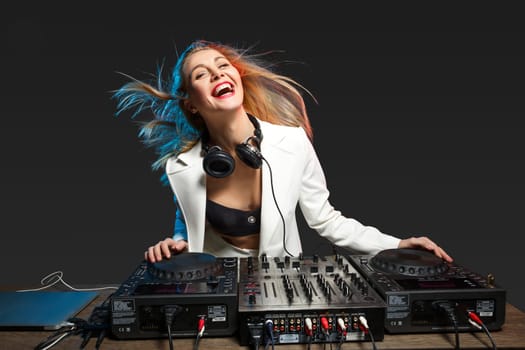 Beautiful blonde DJ girl in a white suit on decks on the party on the black background