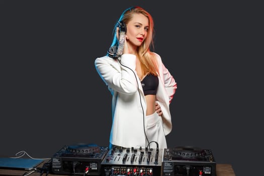Beautiful blonde DJ girl in a white suit on decks on the party on the black background