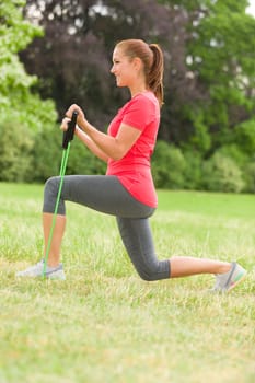 Young woman does stretching exercises with fitness bands in the park.