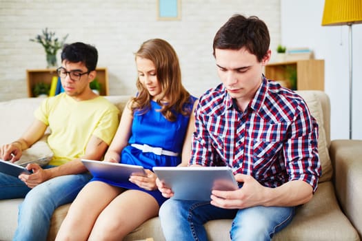Modern guys and girl sitting on sofa with touchpads