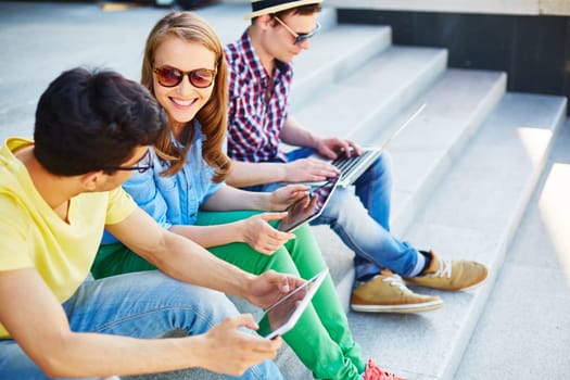 Group of young friends with touchpads and laptop communicating outdoors