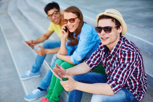 Two guys with touchpads and girl with cellphone spending leisure outdoors