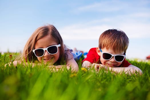 Friendly boy and girl in sunglasses relaxing in green grass