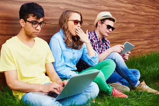 Two guys with touchpad and laptop networking outdoors with bored girl between them
