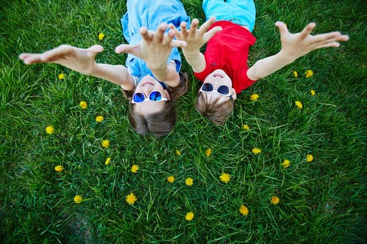 Carefree children in sunglasses lying on green lawn with yellow dandelions
