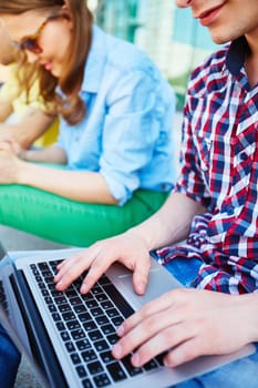 Modern teenager typing outdoors with his friends on background