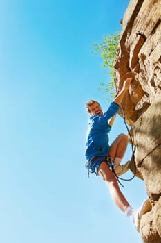 Young mountain climber reaching top of rock