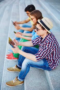 Two guys with touchpads and girl with cellphone sitting on stairs outdoors