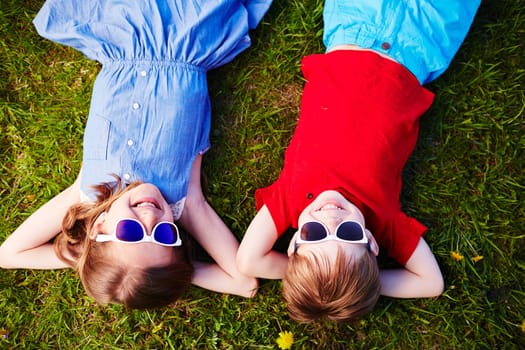 Carefree children in sunglasses relaxing in green grass