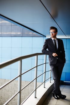Serious businessman in suit standing by railings