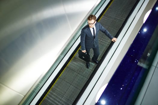 Attractive businessman with briefcase standing on escalator