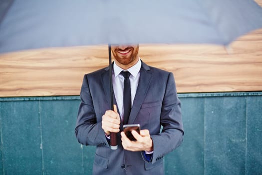 Smiling employee with smartphone standing under umbrella
