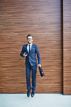 Happy businessman with briefcase and cellphone jumping and looking at camera