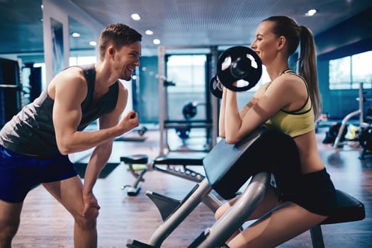 Young woman strengthening arm muscles in gym, her trainer encouraging her