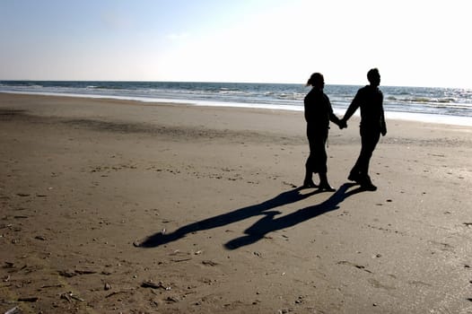 silhoutte of couple walking along the beach hand in hand