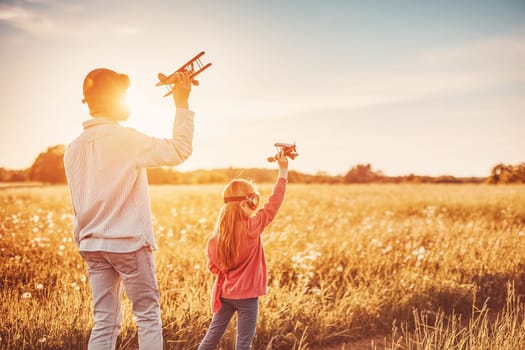 Father with his child playing with toy of plane on the evening field. Concept of love and family vacation.
