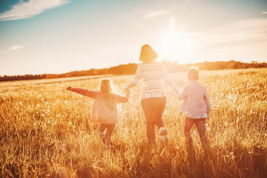 Mother with her children running on the field on the summer sunset. Concept of the family relationship and vacation.