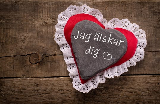 Heart shape of dark slate with the Swedish inscription Jag älskar dig, I love you, on a red fabric heart shape