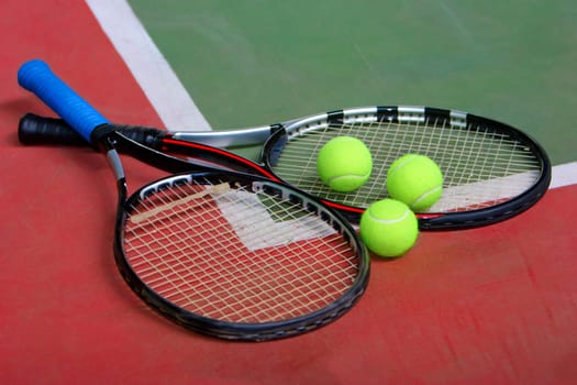 Two tennis racket and three balls on the indoor court.
