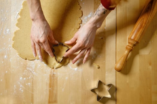Unrecognizable woman cuts out biscuits from dough with cookie cutter