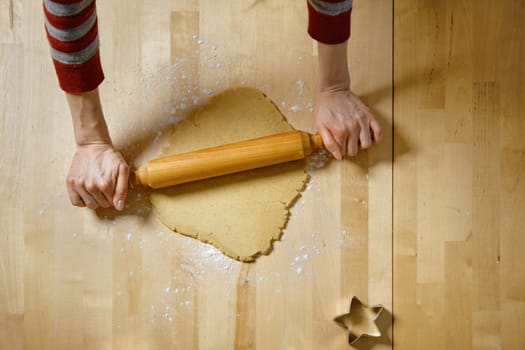 Top view at unrecognizable woman rolling out dough with rolling pin. A woman makes ginger cookies at home.