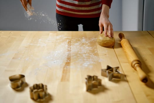 Unrecognizable woman sprinkles flour on table to roll out dough