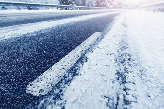 Diminishing perspective of the close-up view of the asphalt road in winter. Icy highway in countryside.