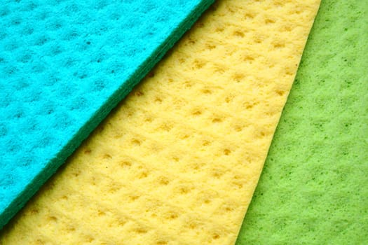 A set of cleaning wipes, microfiber cloths or sponges for the kitchen, three multi-colored cloths. Sponge fibers sponge texture pattern surface close-up background. Green, blue and yellow.