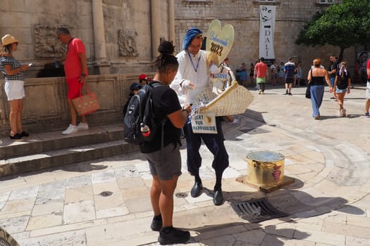 On the streets of Dubrovnik Croatia, happy vacationers walk and buy souvenirs from the seller in the national festive Croatian costume on August 15, 2022. Tourism industry. Summer day. Sale of goods.