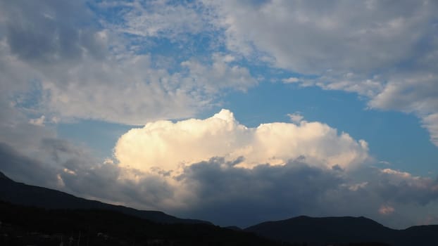 Clouds in the evening sky. The sun's rays pierce the clouds. Blue, yellow and gray colors of the sky and clouds. Beautiful landscape. The sun goes down. Storm weather forecast. Cumulus clouds.