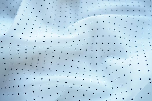 Texture of silk fabric. Black polka dots on a white background. Dress lightweight synthetic fabric in white with a repeating pattern. The textile is made up of waves and folds. Feminine classic style