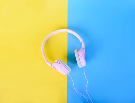 Top view of pink headphones on yellow and blue pastel background. Flat lay music and sound design. Listen to music minimal concept.