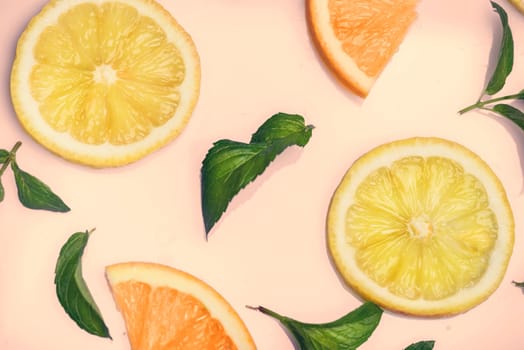 Citrus slices and mint herbs pattern on retro pink background from above. Top view of orange and lemon fruit slices on pastel background.