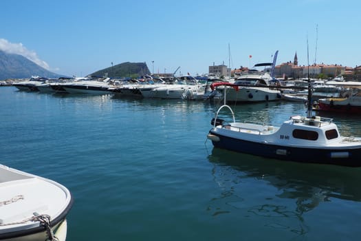 Budva, Montenegro, August 15 2022 Adriatic sea, coast, mountains, sea ripples. Boats and ships are moored to the embankment. Water transport parking. Summer resort trips with tourist water activities.