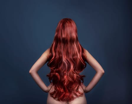 Woman with perfect curly dyed hairstyle from behind. Fashion portrait of red head woman from the back over dark background. Perfect long red hair.