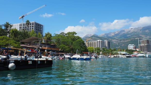Budva, Montenegro, August 15 2022 Adriatic sea, coast, mountains, sea ripples. Boats and ships are moored to the embankment. Water transport parking. Summer resort trips with tourist water activities.