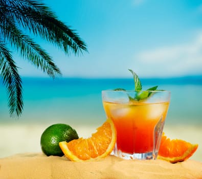 Orange cocktail and citrus fruit on tropical sandy beach. Summer holiday and beach party design.