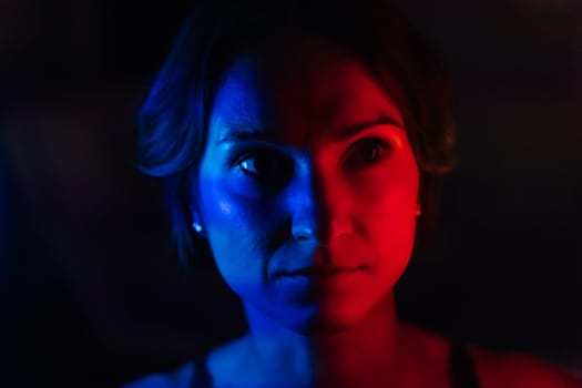 The face of a young woman in blue and red neon light on a dark background.