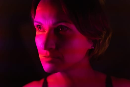 Close-up portrait of a young woman illuminated by stripes of pink and red.