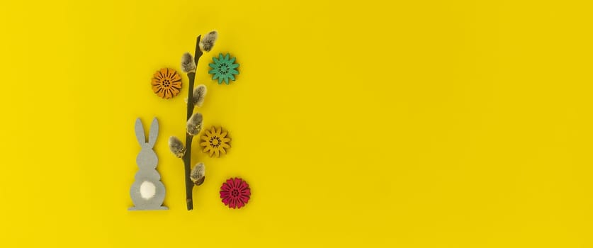 Minimalistic Easter holiday or spring background with Easter Bunny figure, pussy willow branch over a yellow background. Copy space for your text