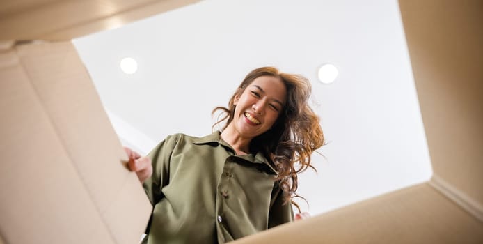 Happy Asian young woman opening carton box from internet store order shopping online at home, Smiling female surprised unpacking christmas gift big box and looking inside, inside bottom view