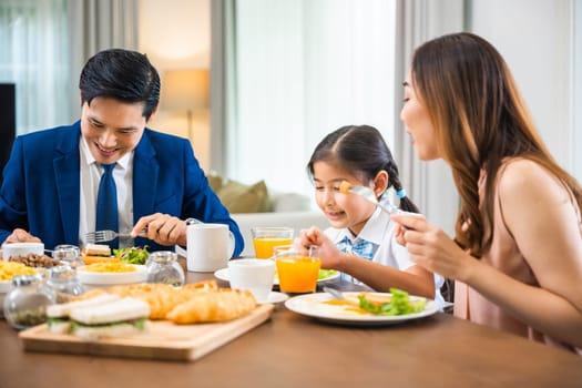 Asian family father, mother with children daughter eating breakfast food on dining table kitchen in mornings together at home before father left for work, happy couple family