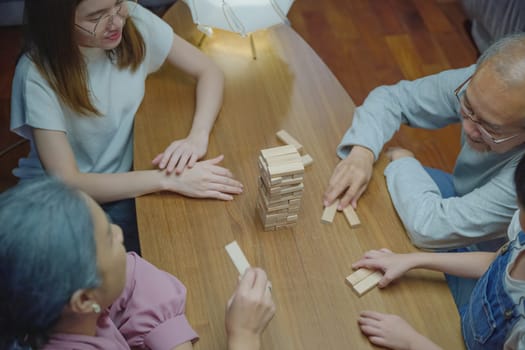 Happy grandparents Asian family enjoy playing toy block with little daughter together in home living room at night time, Smiling parent having fun play build constructor tower of wooden blocks